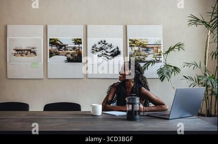 A smiling young woman working at an architectural firm, surrounded by design blueprints and plants. Inspiring an atmosphere of creativity. Stock Photo