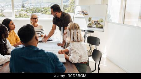 A group of diverse architects, male and female, collaborating on design projects around a table in an architecture studio. Stock Photo
