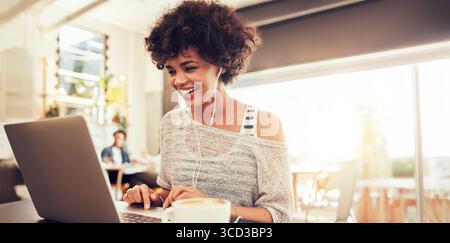 Woman working on laptop in a coffee shop, representing remote work, freelance lifestyle, and digital nomad culture. Ideal concept for online work. Stock Photo