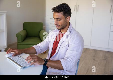 Man typing on wireless keyboard and moving mouse on round table at home office wearing wristwatch Stock Photo