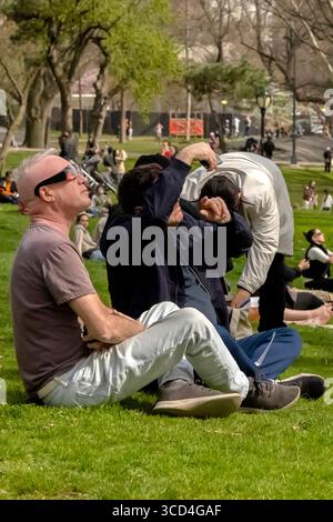 Low-angle view of people observing the April 2024 solar eclipse in Central Park, Manhattan, New York, USA, capturing urban and outdoor life Stock Photo