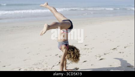 Young african american woman doing cartwheel on beach Stock Photo