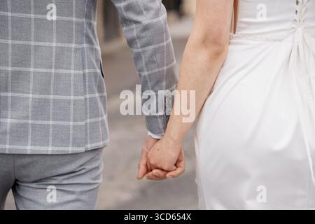 A newlywed couple lovingly holding hands, dressed in formal wedding attire the groom in a gray plaid suit and the bride in a white lace gown suggests Stock Photo
