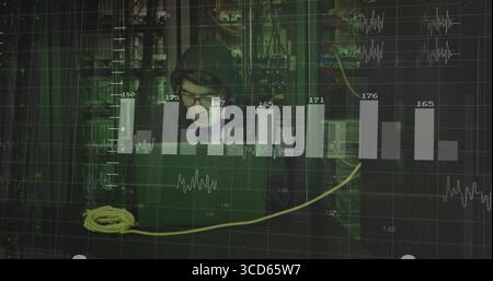 Monitoring data center systems, hooded Korean typing on laptop, with yellow cable and server racks Stock Photo