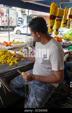 Two florists busy attaching colourful Marigold flower florets into garlands for sale, mainly for Indian celebrations and religious festivals in Chulia Stock Photo