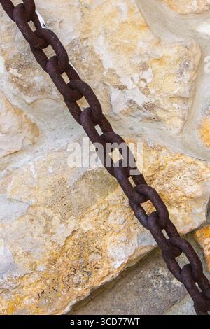 A rusted chain is securely attached to an aged stone wall, showcasing the contrast between the rough textures of the metal and stone in a bright outdo Stock Photo
