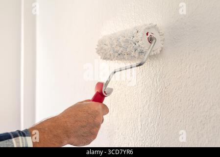 Close-up of a hand. A painter paints a masonry wall with white paint using a roller. Construction industry. Stock Photo