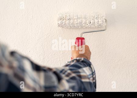 Close-up of a hand. A painter paints a masonry wall with white paint using a roller. Construction industry. Stock Photo