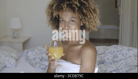 Of a happy african american girl drinking fresh juice on the bed Stock Photo