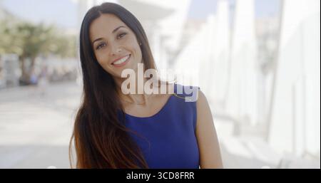 Head and shoulders portrait of a pretty friendly young brunette woman standing outdoors in a high key white urban environment smiling at the camera Stock Photo
