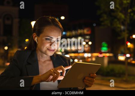 Modern businesswoman working on digital tablet against night city street background Stock Photo
