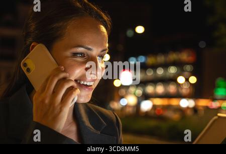 Modern female entrepreneur talking on mobile phone and using tablet on night city street Stock Photo