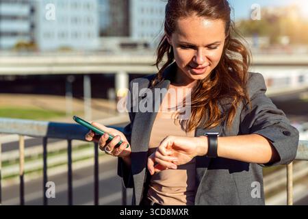 Modern busy woman checking time on smartwatch on background of city. Stock Photo