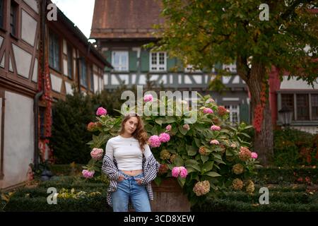 This captivating image showcases a radiant young woman in her early twenties, exuding joy and elegance in a picturesque European garden. Her casual ye Stock Photo
