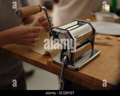 Group of people preparing fresh pasta dough by hand in kitchen, close-up of cooking process, culinary art and traditional noodle making. Stock Photo