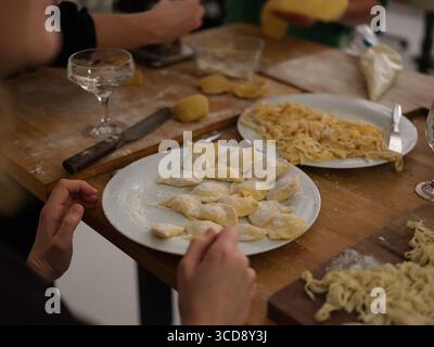 Group of people preparing fresh pasta dough by hand in kitchen, close-up of cooking process, culinary art and traditional noodle making. Stock Photo