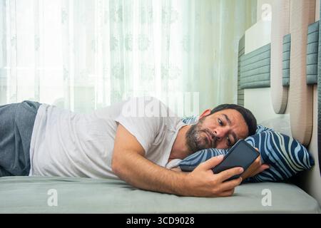 View of man looking at phone in bed as soon as he wakes up Stock Photo