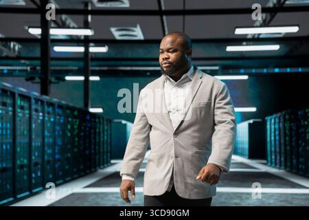 Admin walking in server farm, overseeing infrastructure racks used for managing databases. IT professional in high tech data center doing checkup on server rows storing information Stock Photo