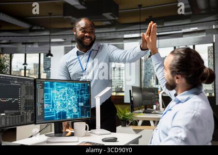 Happy traders doing high five, pleased after gaining money by using AI for stock exchange analysis. Brokerage coworkers celebrating after integrating machine learning analytics to monitor stock market Stock Photo
