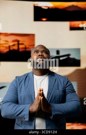 Black person with gratitude standing with hands together in prayer, radiating inner peace and strength for spiritual devotion. Man showcasing peace of mind and divine connection. Stock Photo