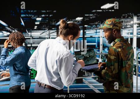 Army technicians using laptop to install server security systems in command center server farm. Military data center engineer and soldier overseeing computer networks for hybrid warfare. Stock Photo