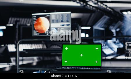 Mockup notebook used for orbital navigation data in cockpit during red planet journey. Green screen laptop used for operating spacecraft control interface next to monitor displaying Mars dashboard Stock Photo
