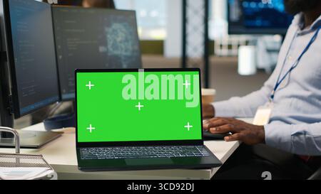 Technician next to office coworkers developing software applications using green screen laptop, integrating AI automation. IT expert debugging applications with mockup notebook, camera A Stock Photo