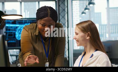 Pleased supervisor recognizing junior dev achievements at work, fostering positive office culture. Cheerful african american manager praising code written by female engineer, doing high five, camera A Stock Photo