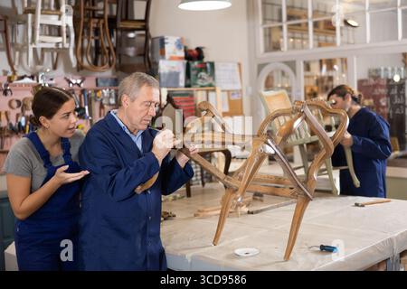 Senior male furniture maker and female apprentice working on vintage commode in workshop Stock Photo