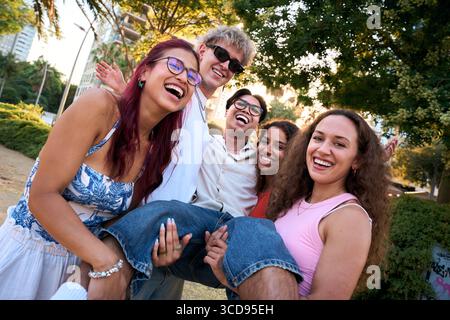 Cheerful students lifting their friend, laughing and having fun in a park Stock Photo