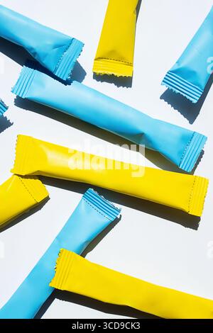 Yellow and blue stick pack sachets scattered on a white background. Doypack packaging for coffee, tea, sugar, spice, food. Stock Photo