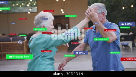 Dancing senior couple exchanging high-five on patio under string lights, with digital notifications Stock Photo