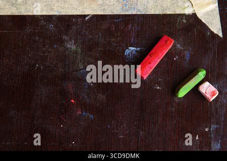 Top view of red and green pastel sticks on a dark wooden table, with masking tape at the top edge. Artistic workspace in progress. Stock Photo