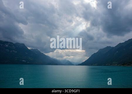 Dramatic sunbeams breaking through stormy clouds over Lake Geneva, surrounded by majestic alpine mountain peaks on a cloudy day. Stock Photo