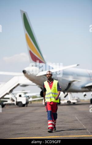 Airport ground crew worker in safety vest walking on runway near airplane, aviation operations, travel industry, airline staff, transportation service Stock Photo