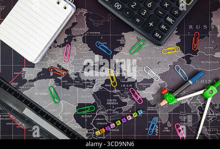 School accessories on dark background. Flat lay with stationery objects on world map background. Back to school concept. Stock Photo