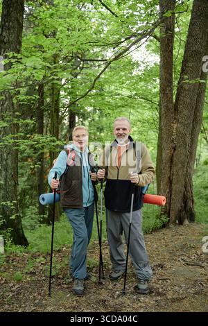 Senior Caucasian Couple Hiking with Trekking Poles in Lush Green Forest Stock Photo
