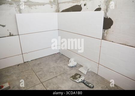 A close up on bathroom renovation with newly laid slip resistant square gray floor tiles and installation of white rectangle ceramic tiles on the wall Stock Photo