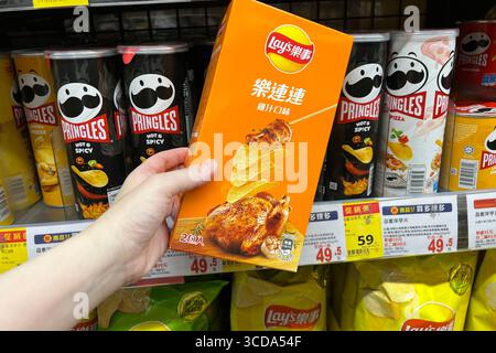 A woman's hand holding potato chips with chicken flavor inside a supermarket Stock Photo