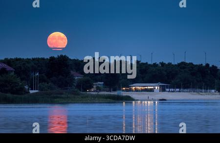Full moon rising in August over the Dnipro River in Kyiv, Ukraine, casting warm reflections on the water Stock Photo