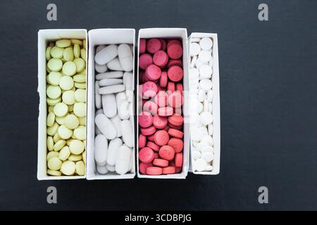 Four packages with multi-colored pills on a black background close-up. Stock Photo