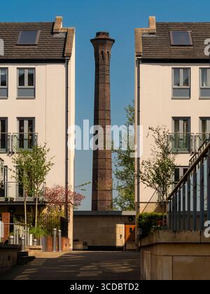 Historic brick chimney on Foss Islands Road in York, framed between two modern apartment buildings under a clear blue sky. York. Stock Photo