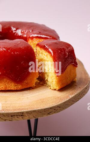 Slice of a vanilla sponge cake with strawberry coulis topping on a wood cake stand. A piece, slice of cake is being served Stock Photo