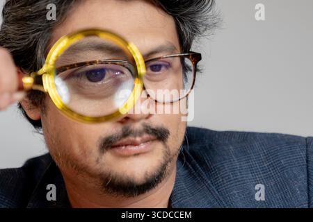 A young man reading a book with a magnifying glass, symbolizing focus and detailed study. Stock Photo