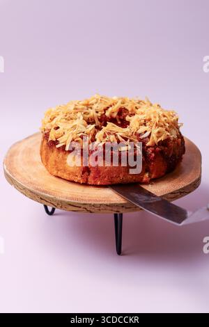 A fresh bundt cake topped with toasted coconut flakes and a rich filling, with a cake server inserted into the side on a rustic wooden stand Stock Photo