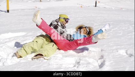 Young couple in ski clothes enjoying a frolic in the snow lying on their backs laughing and kicking their feet in the air Stock Photo