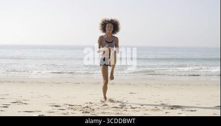 Young sporty african-american woman jumping on the beach in slow motion Stock Photo