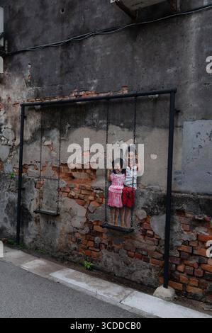 A wall mural of ‘Brother and Sidter’ on a real swing in Lebuh Chulia, (Chulia Street) by Malaysian artist Louis Gan in George Town, a city of Penang i Stock Photo