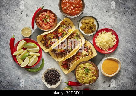 Tasty Mexican meat tacos served with various vegetables and salsa. With sides in ceramic bowls around. Top view composition Stock Photo