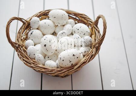Basket of chicken and quail white dotted Easter eggs in brown wicker basket. Placed on white wooden table Stock Photo